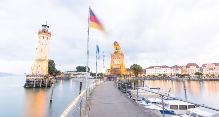 Port avec un phare et des bâtiments historiques sous un ciel nuageux.
