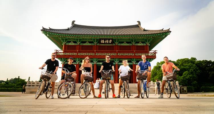 Un groupe de personnes avec des vélos devant un palais coréen.