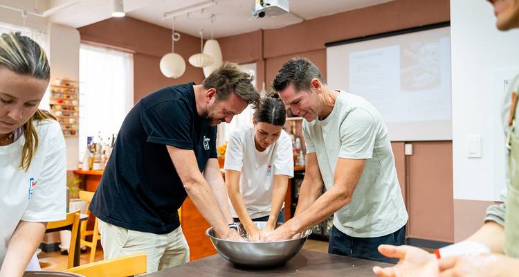 Trois personnes mélangent des ingrédients dans un bol lors d'un cours de cuisine.