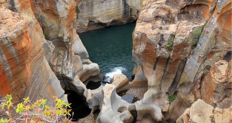 Bird’s-eye view into Bourke’s Luck Potholes where swirling rock formations meet deep green water.