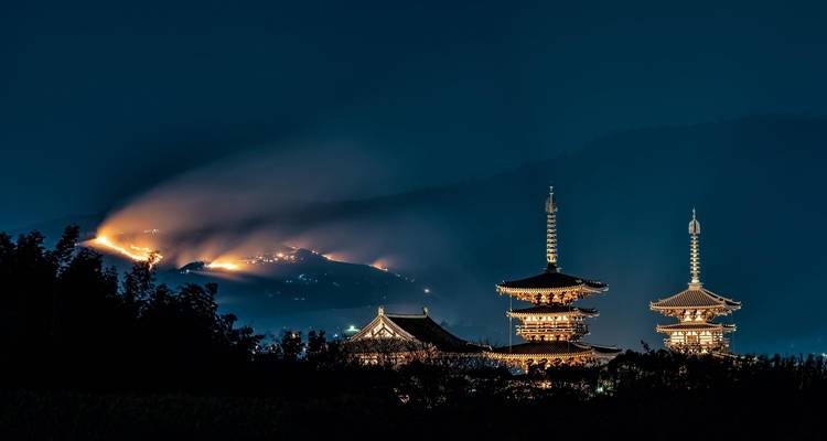 Pagode illuminée avec montagnes lointaines sous un ciel nocturne.