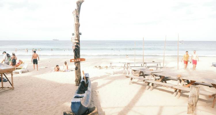 Strand met houten tafels, banken en mensen die genieten van de oceaan.