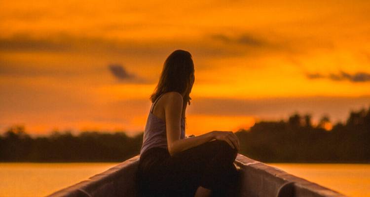 Femme assise à l'avant d'un bateau pendant le coucher du soleil.