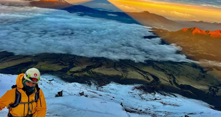 Montañista con chaqueta amarilla contemplando una dramática inversión de nubes y sombra piramidal al amanecer