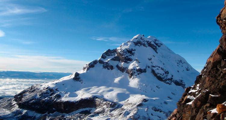 Pico aislado irregular cubierto de nieve contra un cielo azul brillante y una capa de nubes distante