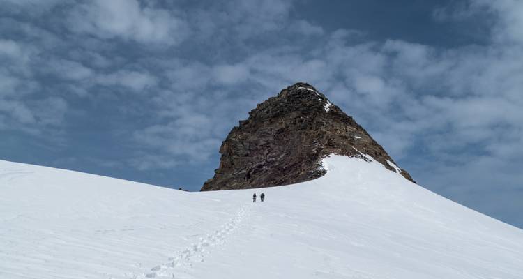 Snow-covered mountain peak with footprints leading to the top.