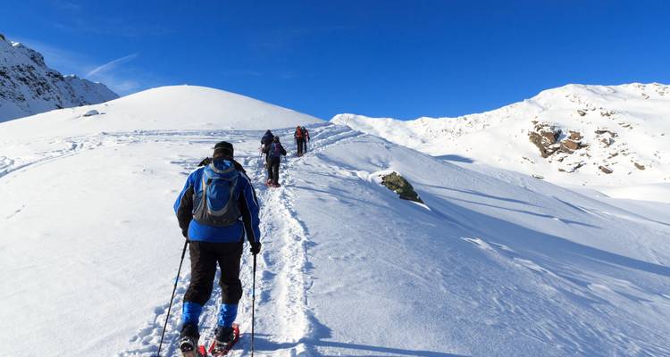 Hikers trekking through snowy mountains under a clear blue sky.