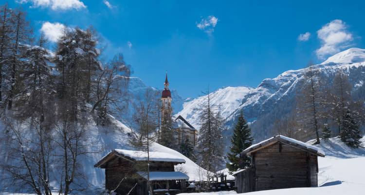 Mountain village with snow-covered houses and a church tower.