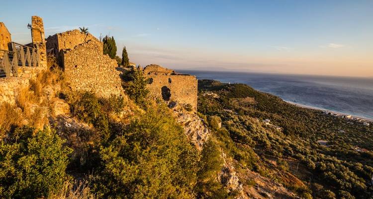 Coucher de soleil sur une falaise côtière avec des ruines historiques et une vue sur la mer.