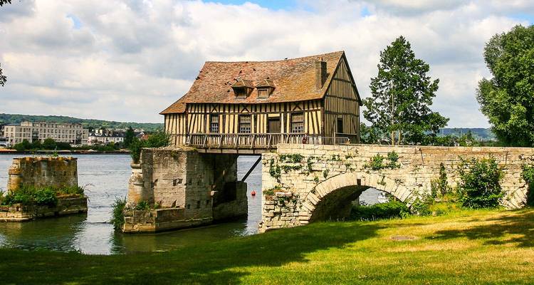 Ancien moulin sur un pont au-dessus d'une rivière avec un paysage pittoresque en arrière-plan.