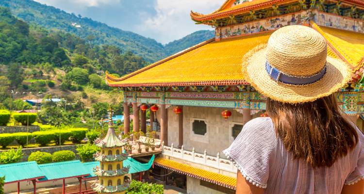Femme regardant un temple traditionnel avec des jardins paysagers.