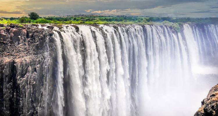 Vue latérale des Chutes Victoria avec d'immenses projections d'eau et une forêt verdoyante luxuriante au-delà