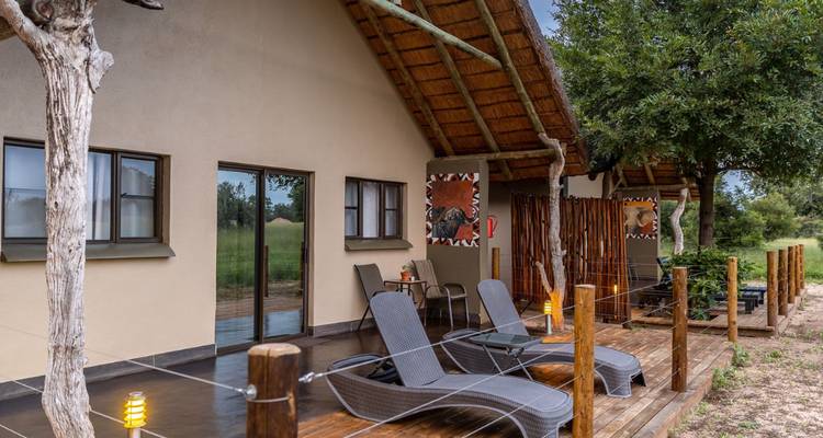 Vista exterior de una cabaña con sillas de descanso en una terraza.