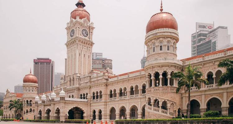 Grand bâtiment Sultan Abdul Samad de l'époque coloniale avec tour d'horloge et dômes de cuivre se détachant sur un horizon urbain moderne.