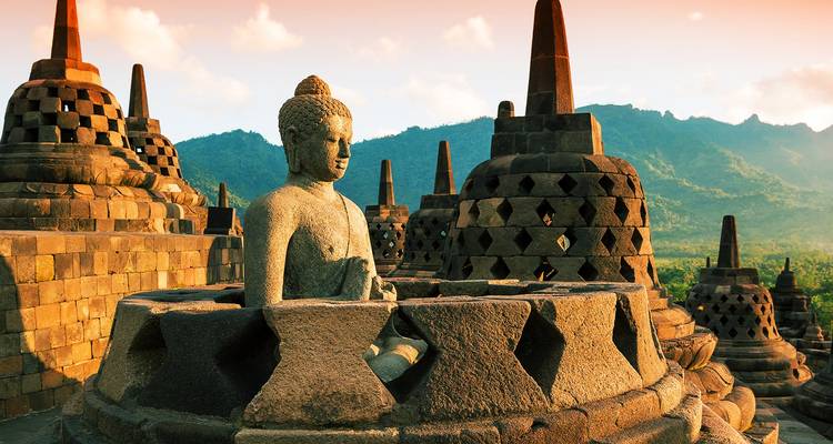 Estatua de Buda de piedra sentada en una estupa perforada al amanecer en Borobudur con montañas brumosas detrás
