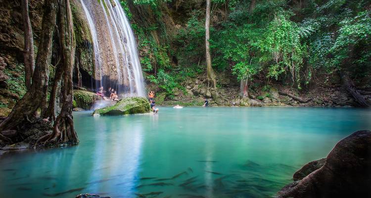 People swimming in a turquoise pool beneath a waterfall.