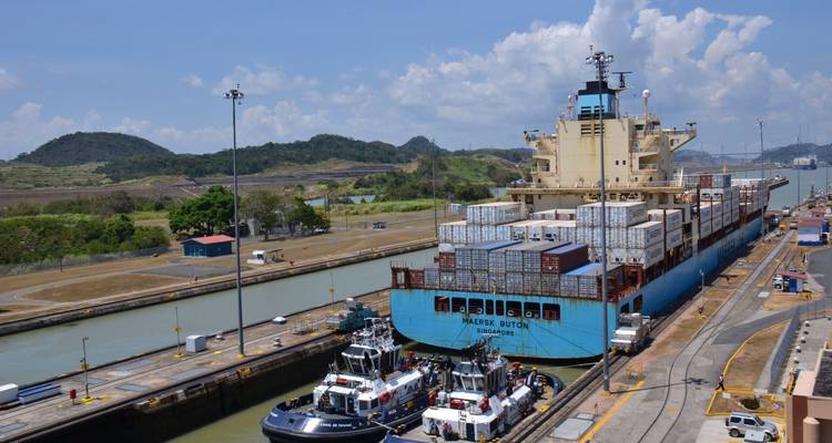 Ein Frachtschiff in einer Kanalschleuse mit üppigen Hügeln ringsum.
