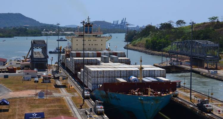 Frachtschiff in einer Kanalschleuse, mit Kränen und Brücken im Hintergrund.