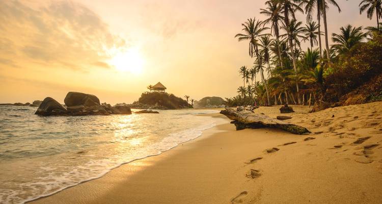 Sonnenuntergangsblick auf einen Strand mit Palmen und einer Hütte.
