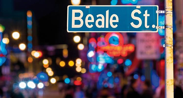 Panneau de Beale Street illuminé la nuit avec des lumières colorées en arrière-plan.