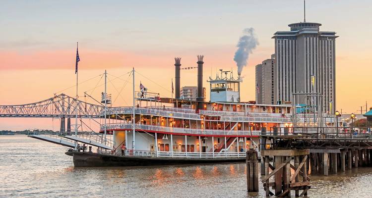 Bateau à vapeur sur une rivière avec un pont en arrière-plan au coucher du soleil.