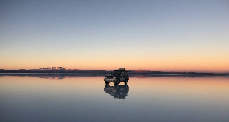 Jeep on reflective salt flats at sunrise.