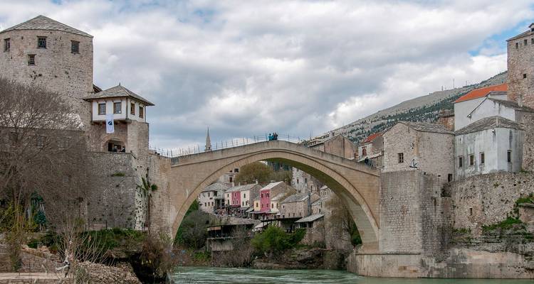 El icónico puente de piedra Stari Most arqueándose sobre aguas turquesas con los históricos edificios de Mostar a ambos lados.
