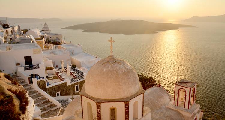 Dôme d'église classique de Santorin surplombant la caldeira au coucher de soleil doré.