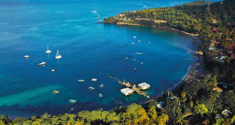 Vue aérienne d'une baie azur avec des yachts et un littoral verdoyant sur une île tropicale.