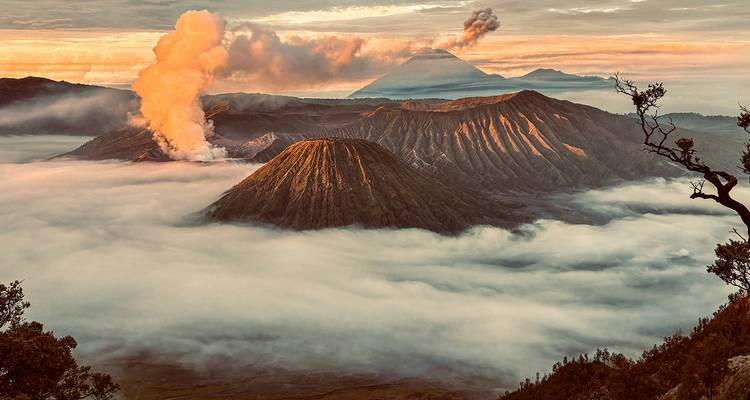 Vue dramatique de montagnes volcaniques avec fumée et nuages au lever du soleil.