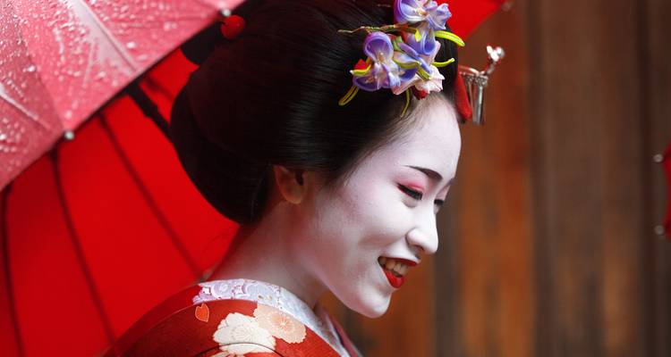 Profil d'une geisha habillée de manière traditionnelle avec un parapluie rouge.