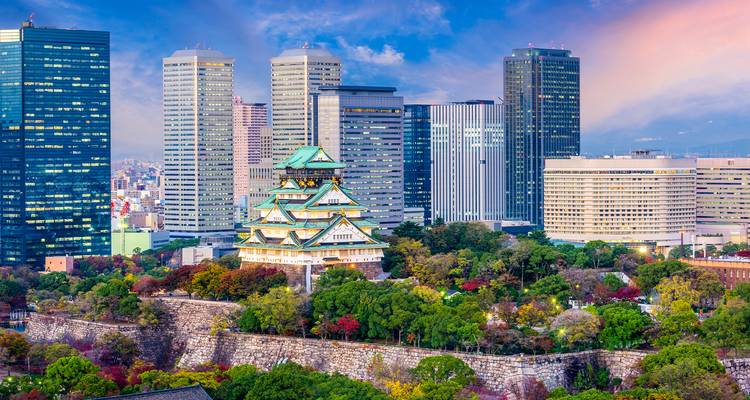 Osaka Castle surrounded by modern skyscrapers and lush green trees.