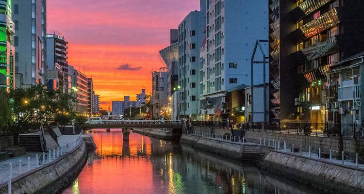 A vibrant sunset over a canal lined with modern buildings.