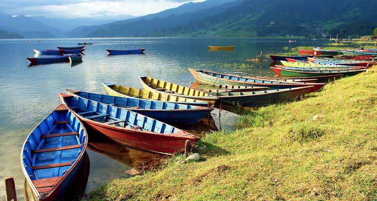 Coloridos barcos de madera alineados en la orilla de un lago con montañas de fondo.