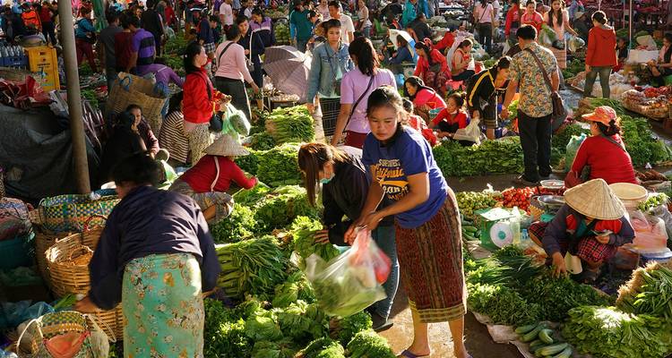 Escena bulliciosa de mercado con gente y una variedad de verduras.