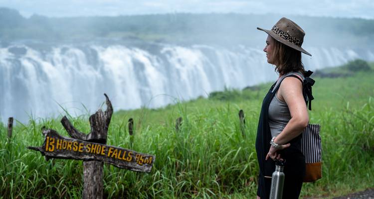 Woman standing beside a large waterfall with a sign pointing to it.