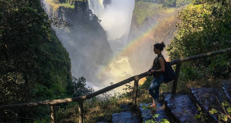 Persona de pie cerca de las cataratas Victoria con un arco iris.