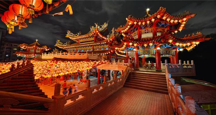 Temple chinois aux couleurs éclatantes et cour remplie de lanternes rayonnant contre un ciel nocturne sombre.