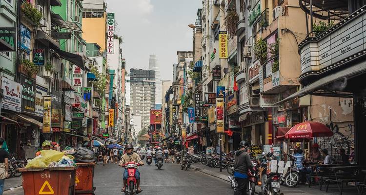 Scène de rue animée avec des motos et des enseignes colorées dans une zone urbaine.