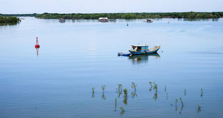 Scène sereine d'un bateau sur une étendue d'eau calme avec quelques huttes en arrière-plan.