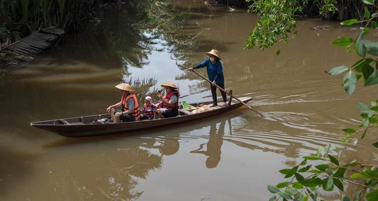 Three people in a boat on a calm river surrounded by vegetation.