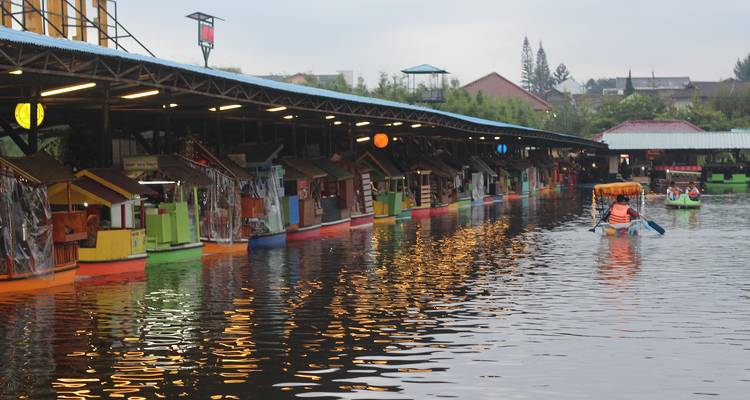 Floating market shops lined up along a river, with people in small boats.