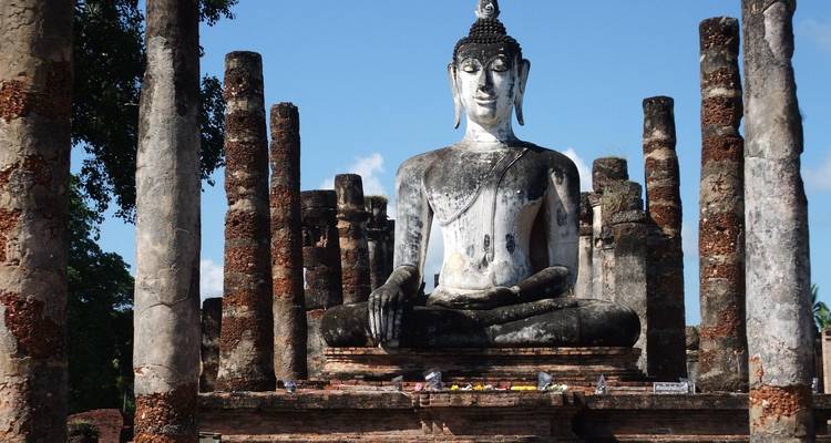 Large Buddha statue amidst ancient ruins with blue sky.
