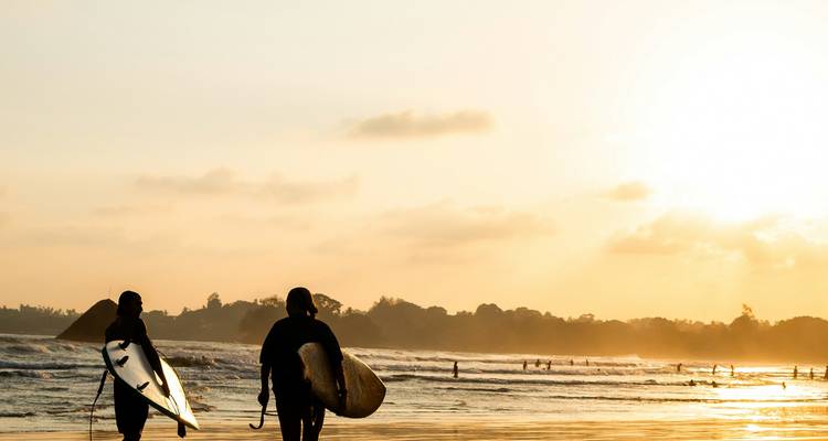 Siluetas de surfistas caminando en la playa al atardecer.