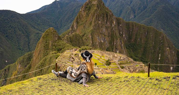 A woman sitting on a mountain ridge with a view of the Machu Picchu ruins.