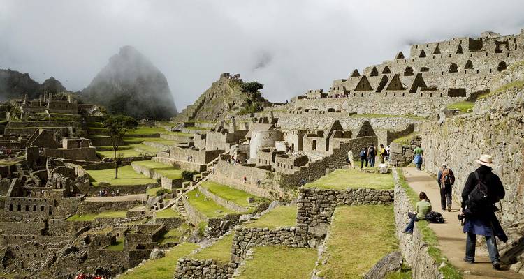 Tourists exploring the ruins of Machu Picchu under a cloudy sky.