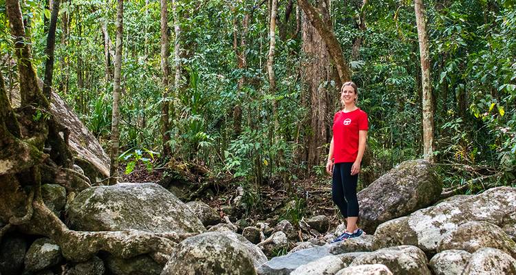 Woman in red shirt hiking through a rainforest trail.