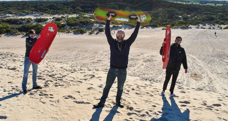 Trois personnes tenant des planches de sable sur une dune de sable.