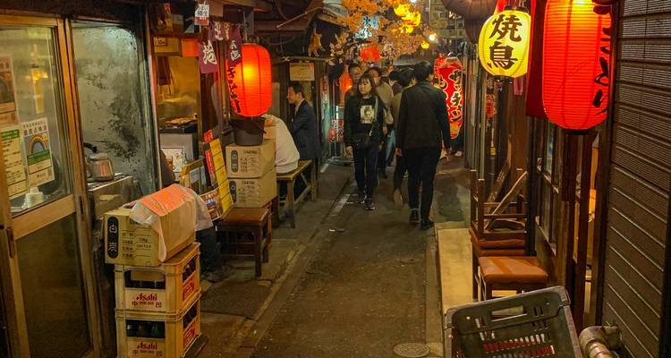 Eine schmale Gasse mit beleuchteten roten Laternen und gehenden Menschen.