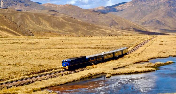 Tren viajando a través de un paisaje montañoso junto a un río.